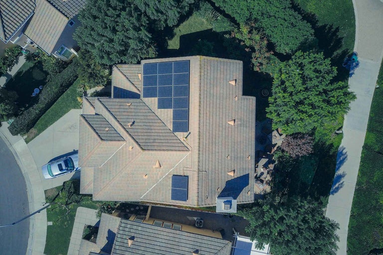 Vedere aeriană a unei case cu acoperiș din țiglă și panouri solare într-o zonă rezidențială.