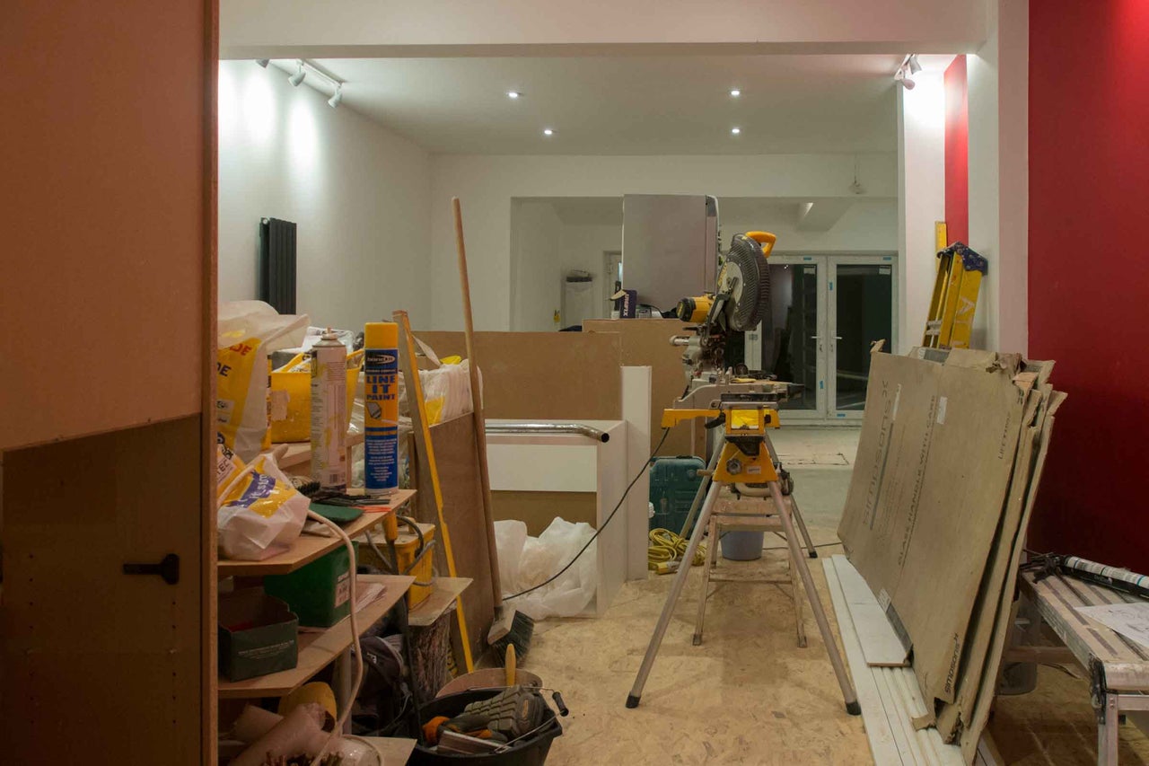 Șantier luminos în timpul unei renovări cu un ferăstrău circular staționar pe un suport, materiale de construcție, unelte și o scară.