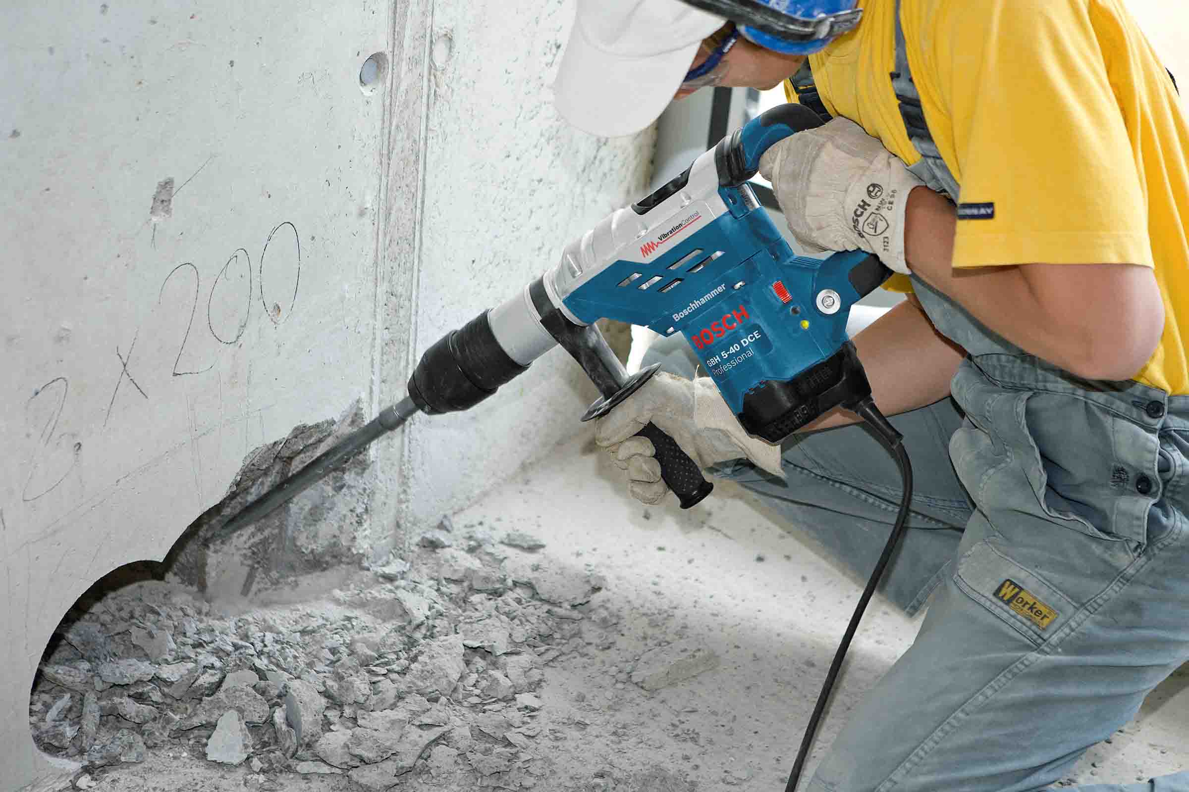 Un muncitor forează o gaură într-un perete de beton cu un ciocan rotopercutor Bosch.