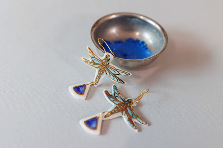 Doi cercei libelulă cu accente albastre și un bol în fundal.