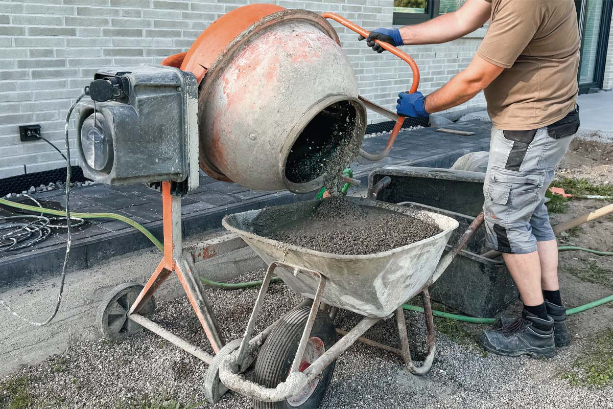 Un muncitor toarnă beton proaspăt amestecat dintr-o betonieră într-o roabă pe un șantier.