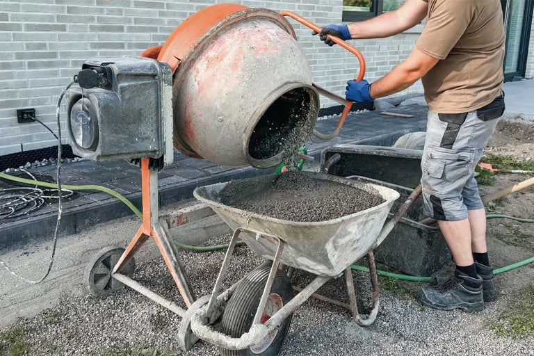 Un muncitor toarnă beton proaspăt amestecat dintr-o betonieră într-o roabă pe un șantier.