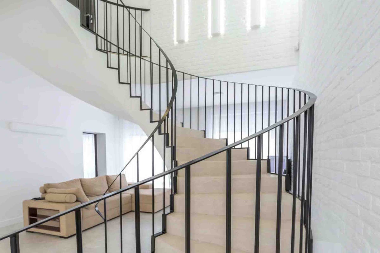 Scară în spirală modernă cu trepte din piatră și balustradă din metal negru într-o cameră de zi luminoasă și deschisă.