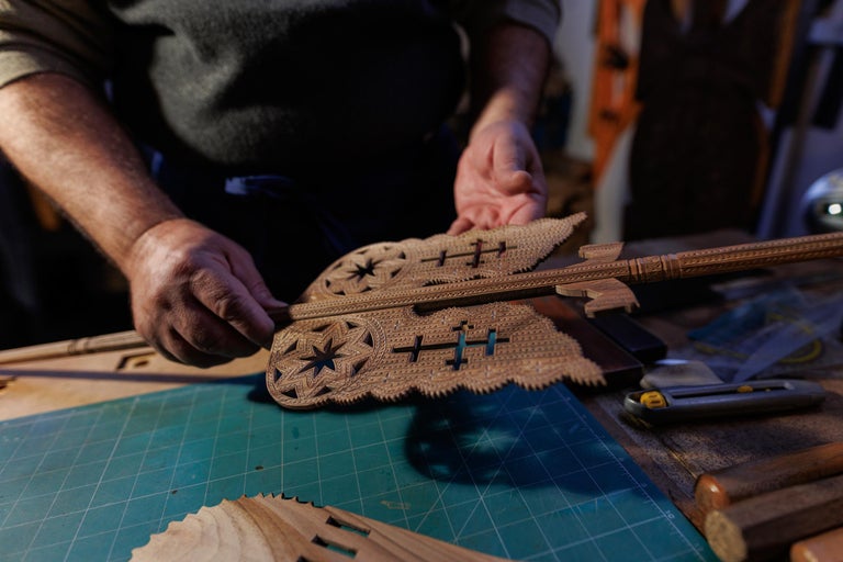 Prim-plan cu o persoană care ține un obiect din lemn sculptat filigranat, prezentând măiestrie tradițională și sculptură detaliată în lemn