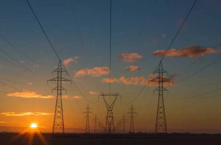 Stâlpi de înaltă tensiune cu linii electrice aliniați în timpul unui apus de soare.
