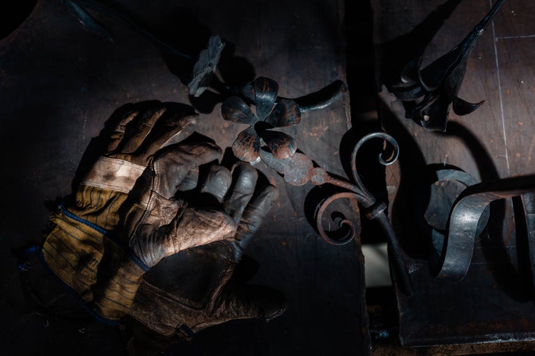 Mănuși de protecție și flori metalice realizate manual pe un banc de lucru.