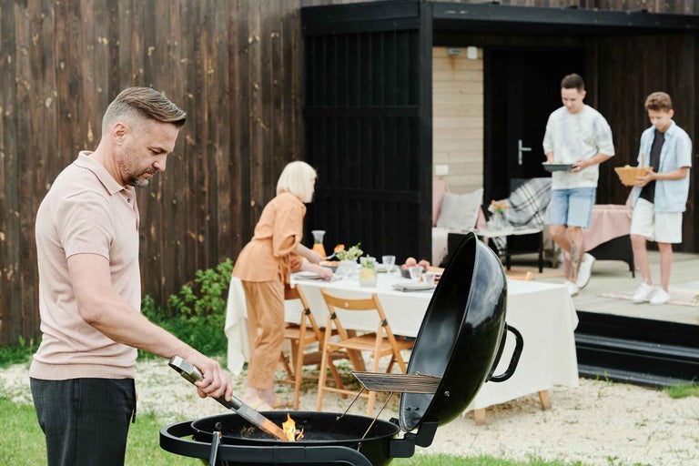 Scenă de grădină cu un grătar și o familie care pregătește o masă.