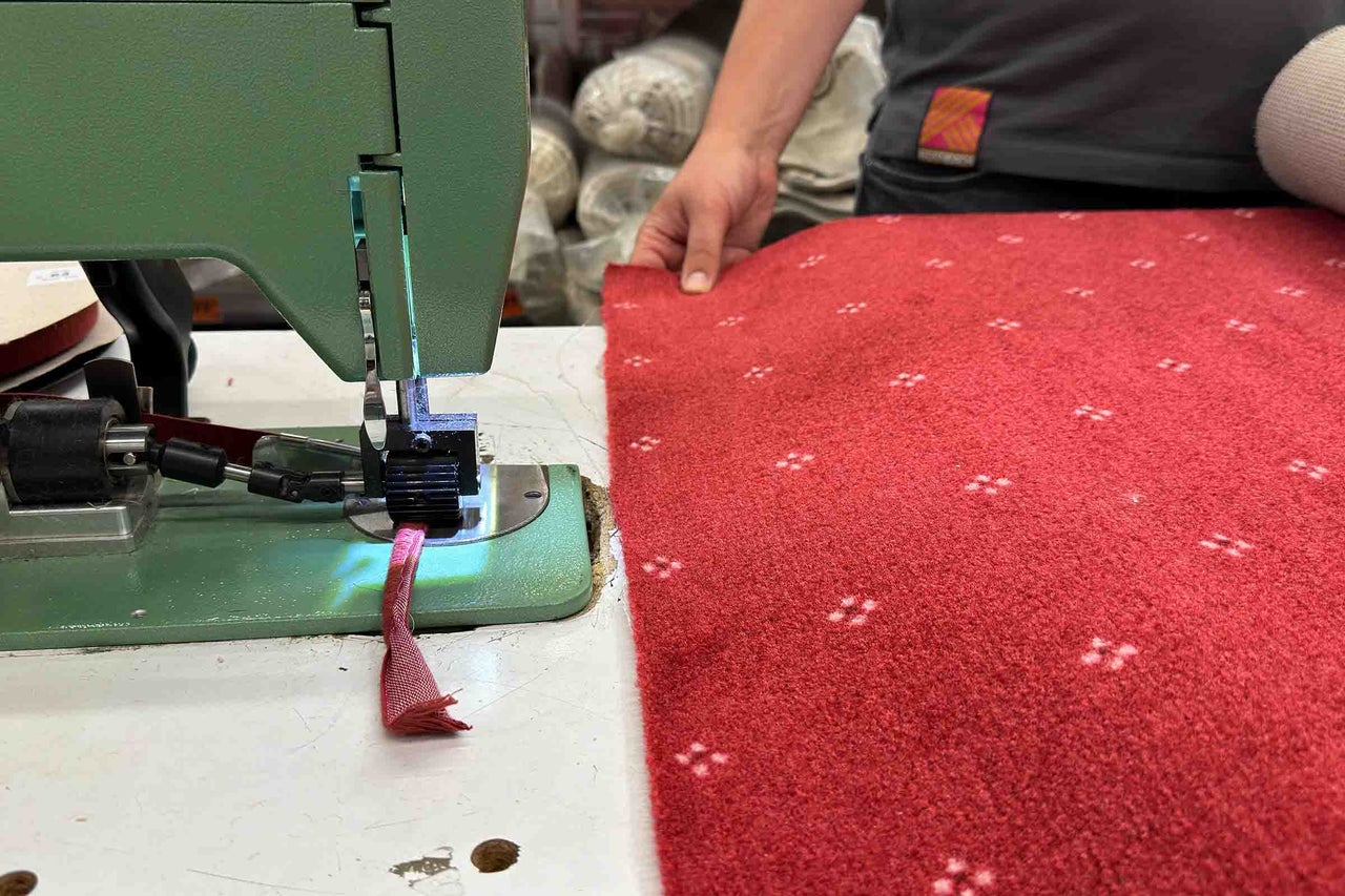 O mașină de cusut verde tiveste un covor roșu cu model.