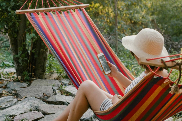 Femeie se relaxează într-un hamac în dungi și folosește un smartphone