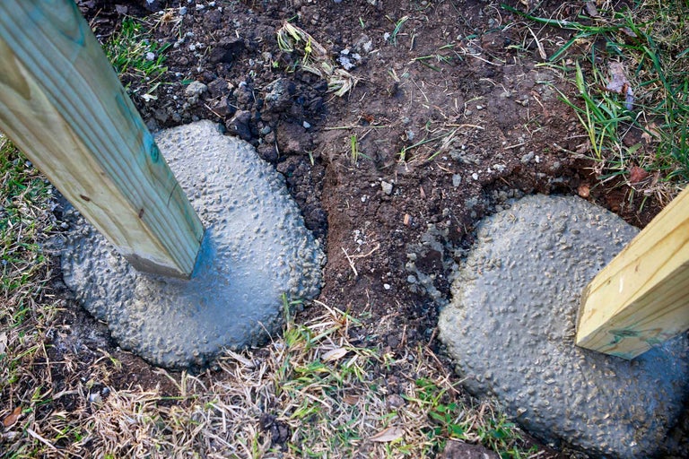 Doi stâlpi de lemn în fundații de beton în grădină.