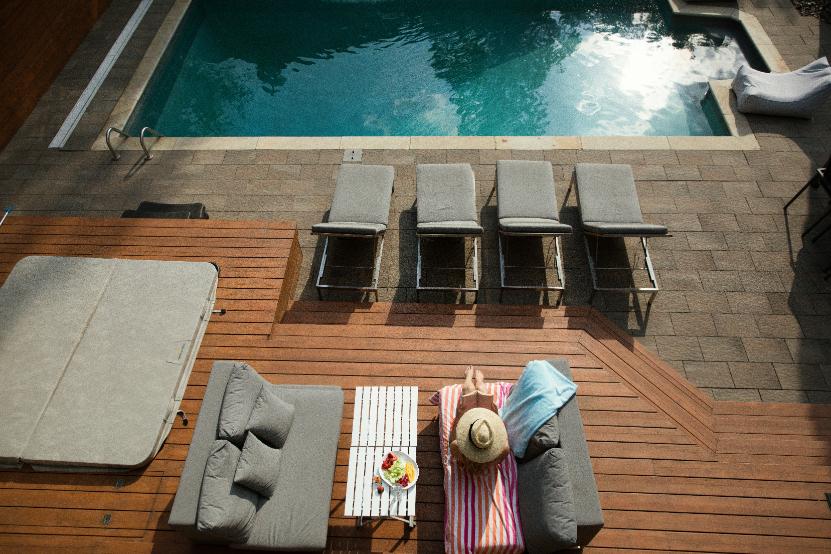 Vedere de sus a unei terase cu piscină, șezlonguri, jacuzzi și o persoană pe un șezlong