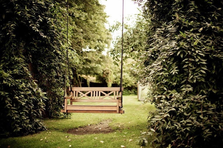Leagăn de lemn atârnat de frânghii între copaci în grădină.