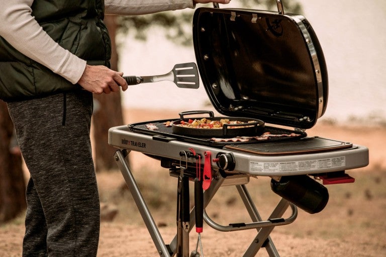 Bărbat care face grătar în aer liber pe un grătar Weber Traveler.
