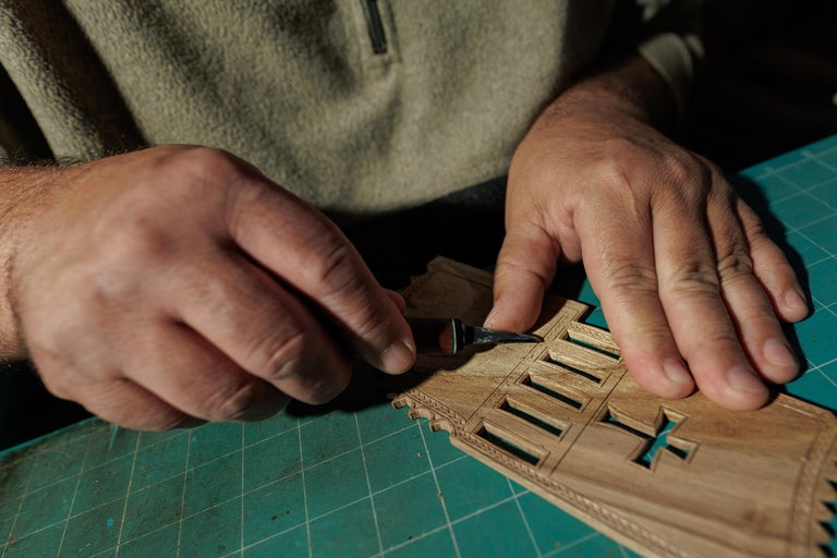 Prim-plan cu o persoană care lucrează la un model din lemn cu un cuțit pentru hobby.