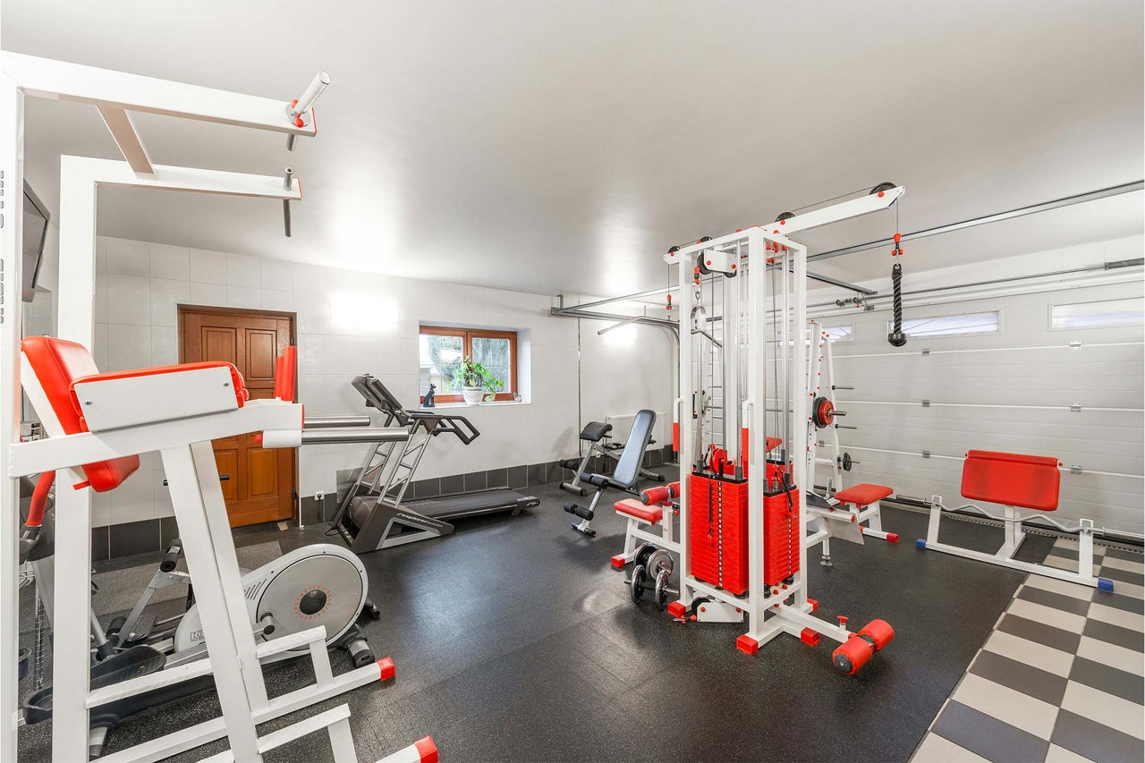 Sală de fitness cu diverse echipamente de antrenament, cum ar fi stație multifuncțională, bandă de alergare și bancă de haltere.