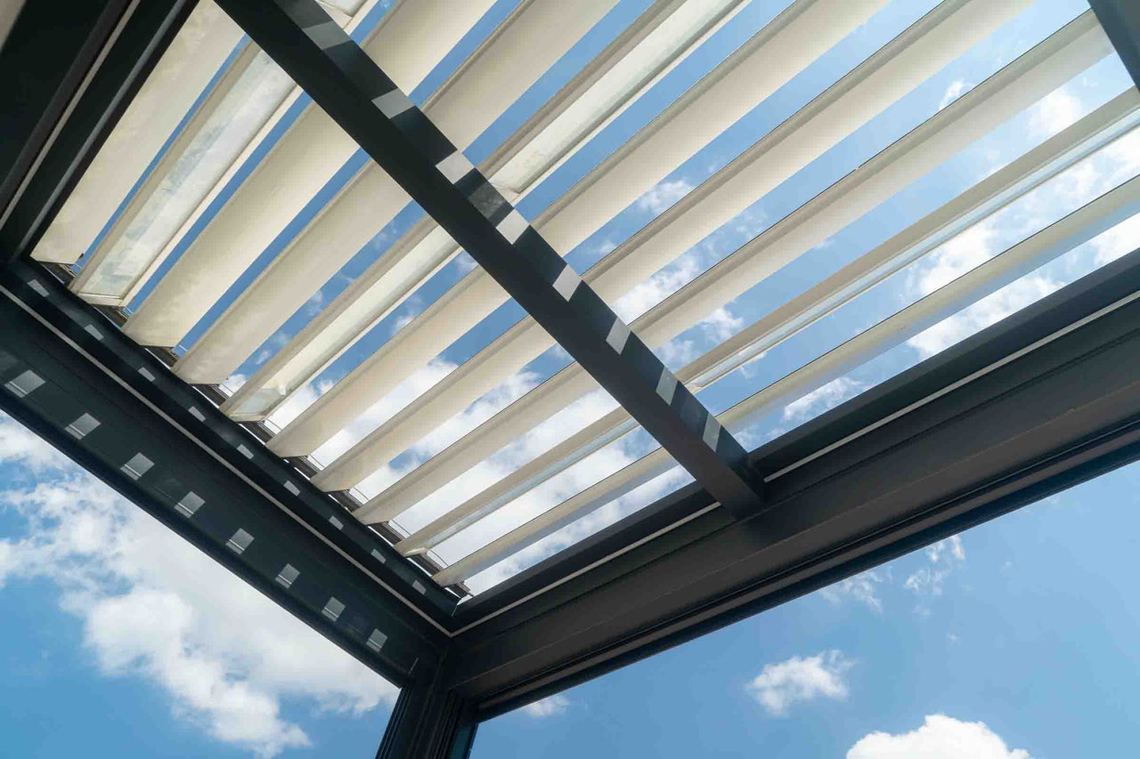 Lamele reglabile ale unui acoperiș de terasă modern din aluminiu, cu vedere spre cer.