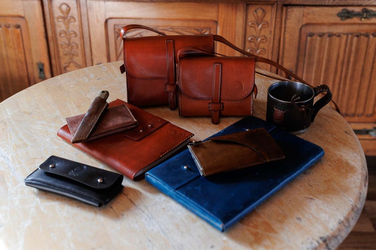 Diverse produse din piele, inclusiv genți, caiete și un cuțit, pe o masă