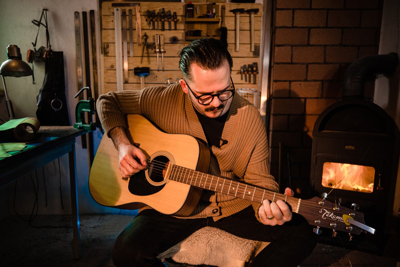 Bărbat cântând la chitară acustică într-un atelier cu scule și sobă