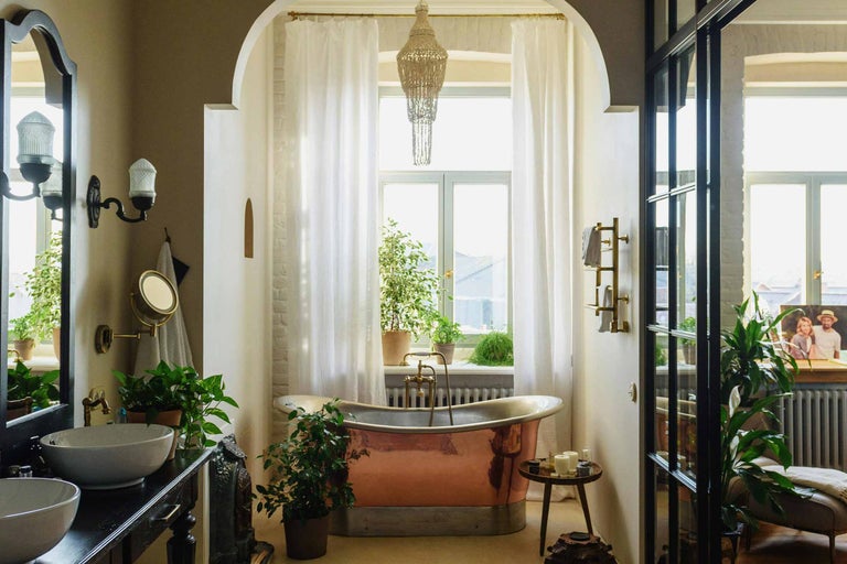 Baie cu cadă, chiuvetă, oglindă, fereastră și elemente decorative, cum ar fi plante și o lampă suspendată