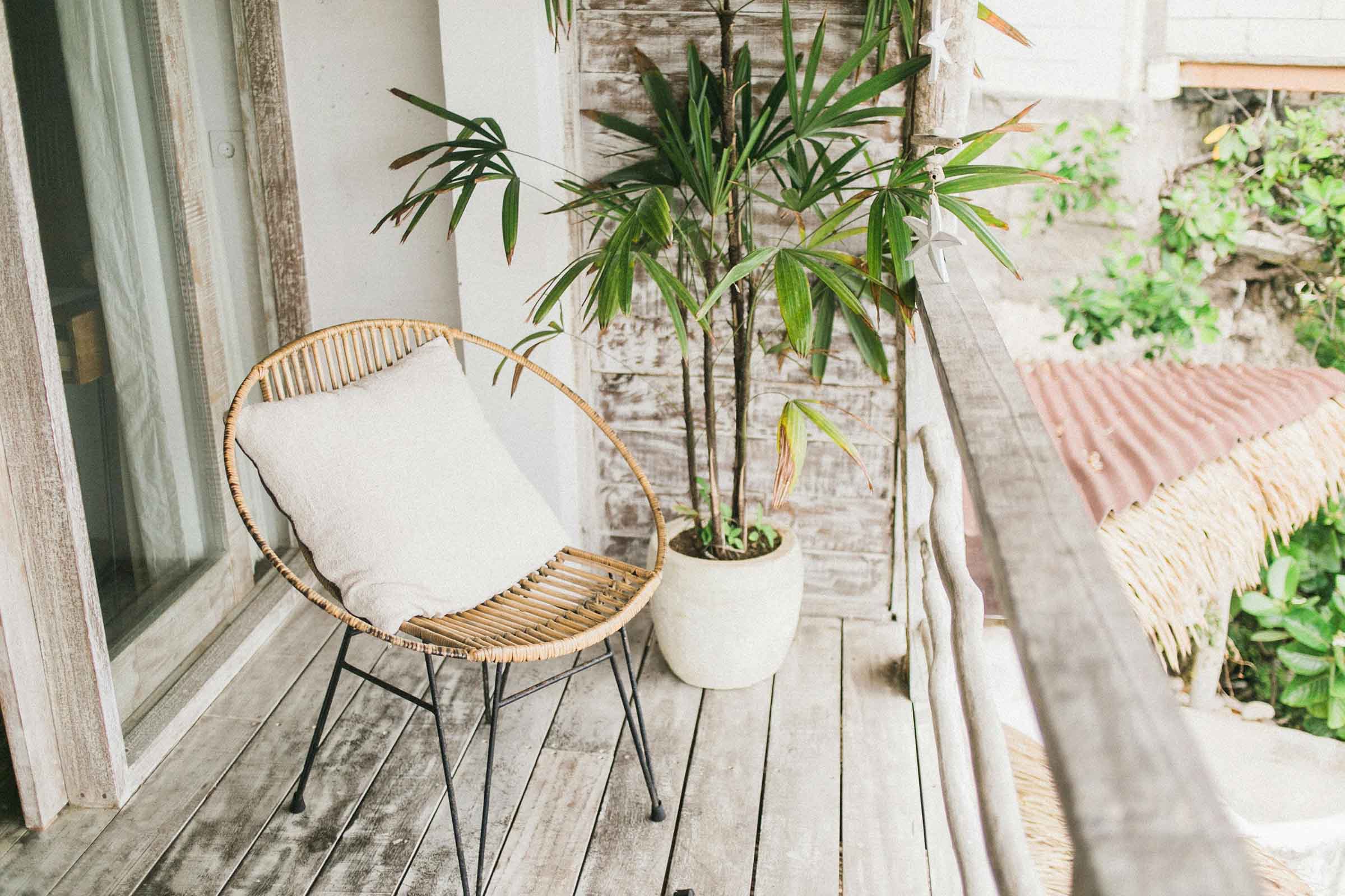 Scenă cu un scaun de ratan, o pernă și o plantă în ghiveci pe un balcon.