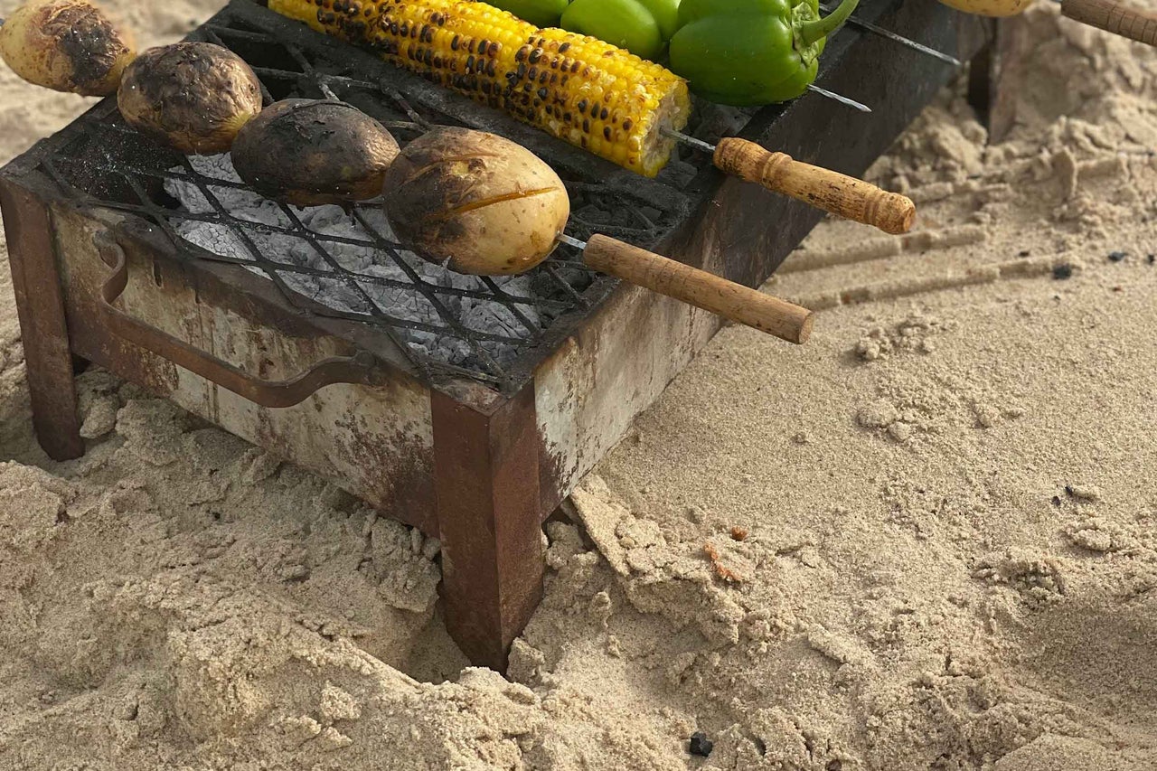 Legume precum cartofi, porumb și ardei pe un grătar pe plajă