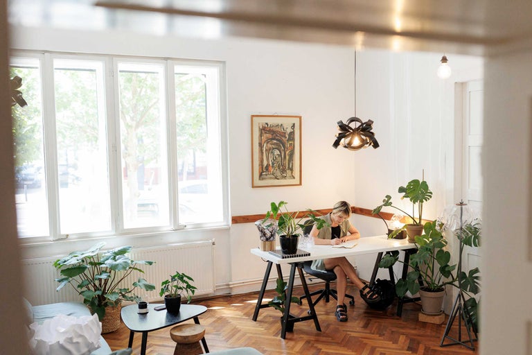 Birou luminos cu birou, scaun, plante de interior și o femeie care scrie