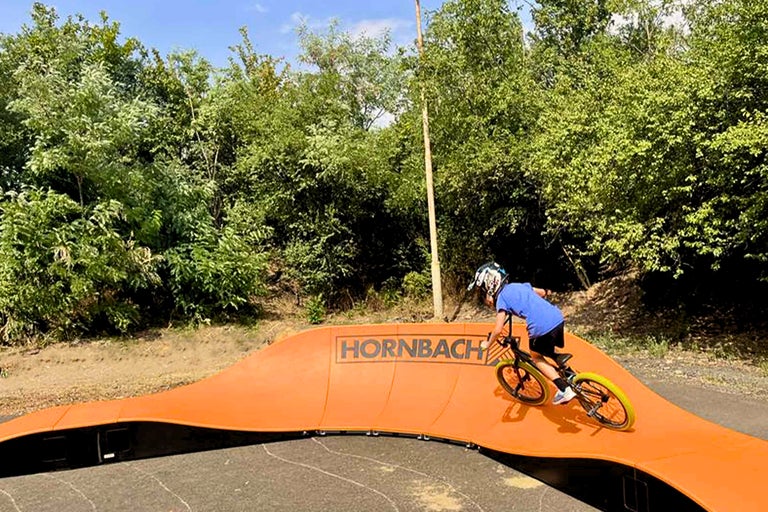 Băiat care merge cu bicicleta pe un pumptrack cu sigla Hornbach.