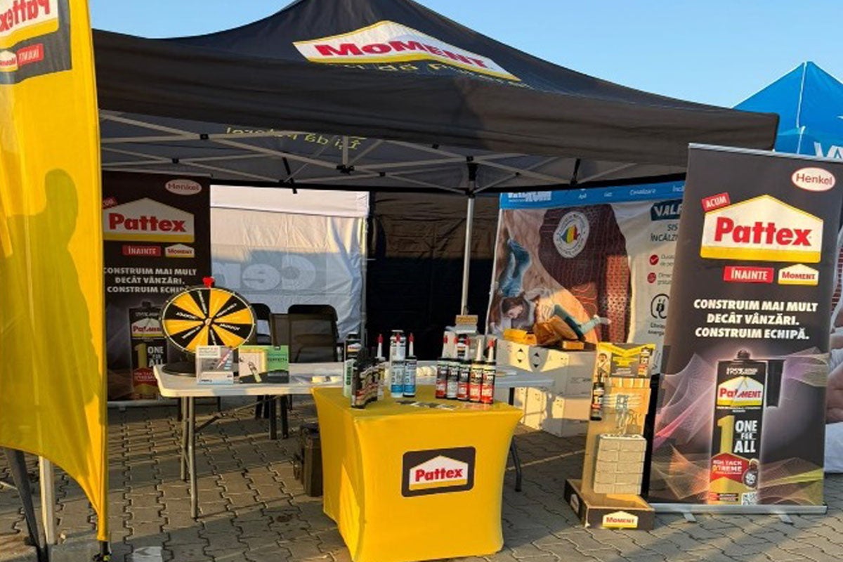 Stand promoțional Henkel cu produse Pattex și Moment sub un pavilion cu bannere publicitare, Pattex Logo, Moment Logo și o roată a norocului.