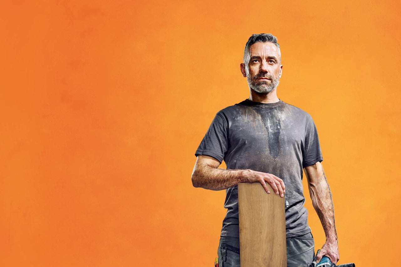 Un bărbat cu o scândură de lemn pe un fundal portocaliu.