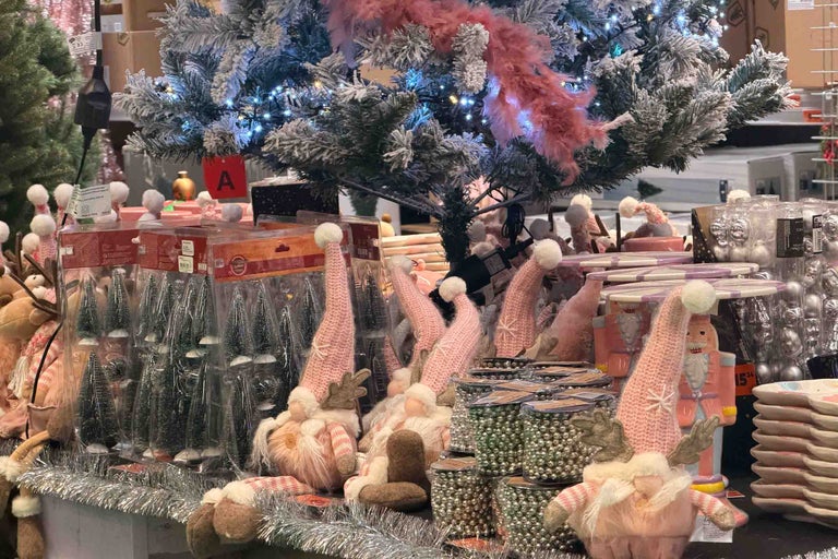 Decoratiuni de Craciun pe raftul unui magazin cu figurine pitici, brazi artificiali si siraguri de margele stralucitoare sub un brad inzapezit