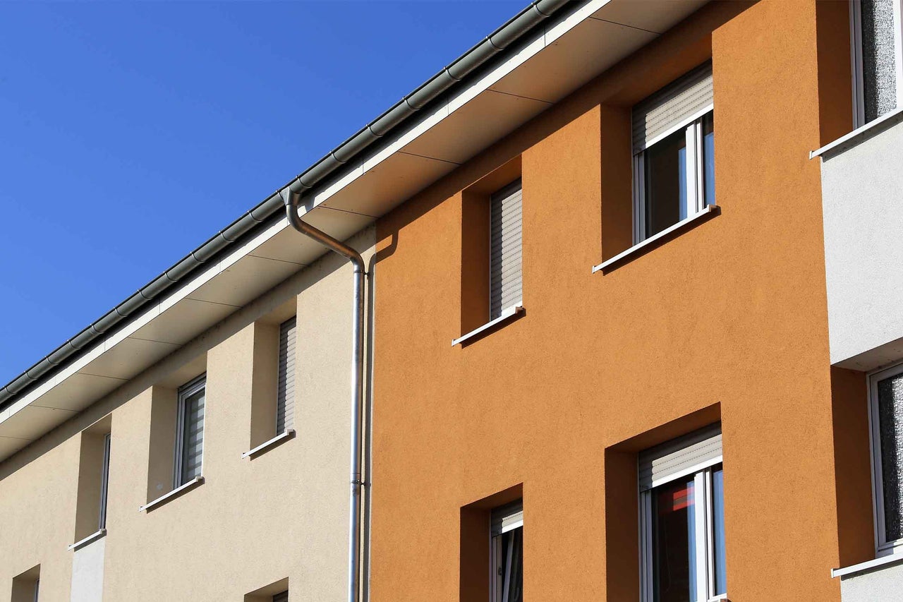 Fațadă modernă de casă cu tencuială exterioară portocalie și bej, ferestre cu rame albe, jaluzele exterioare și un jgheab argintiu.