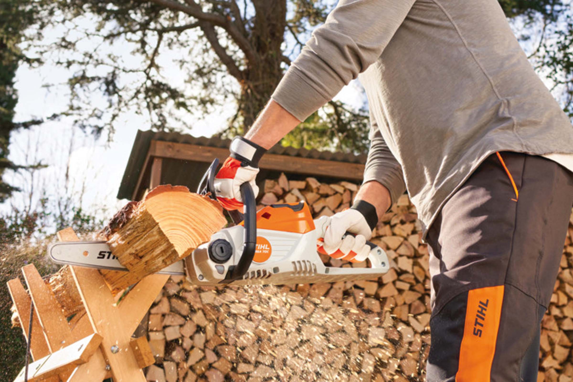 Bărbat taie lemne cu un ferăstrău electric cu acumulator Stihl pe un cal de tăiat lemne