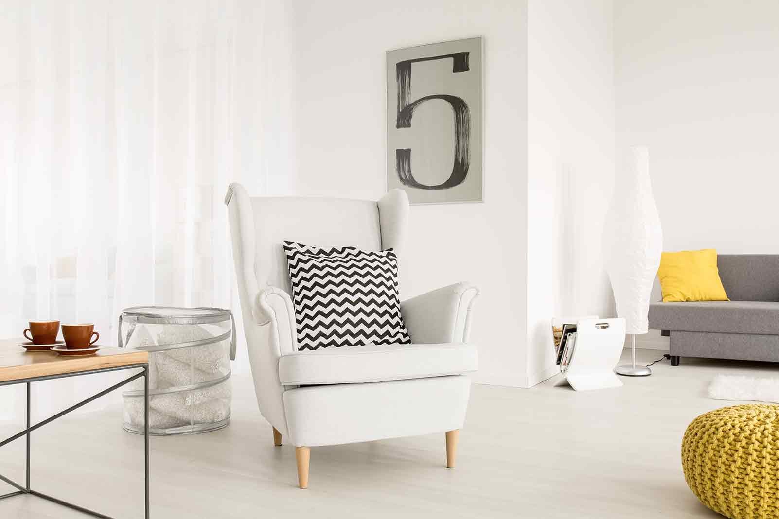 Cameră de zi luminoasă cu fotoliu, canapea, măsuță laterală și obiecte decorative pentru o ambianță confortabilă