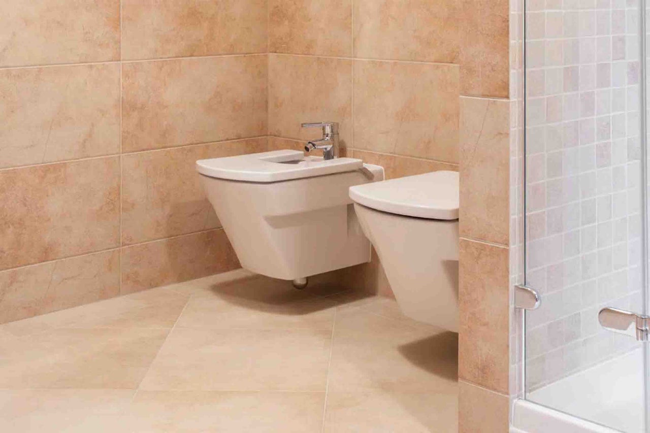 Bideu și WC suspendate din ceramică albă într-o baie cu gresie și faianță bej.