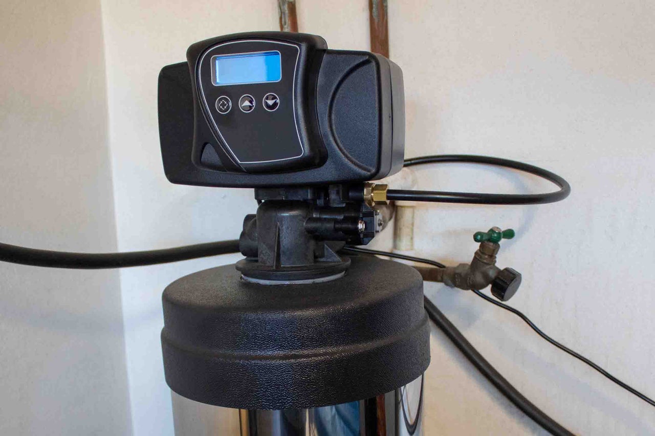 Sistem de dedurizare a apei cu unitate de control digitală și afișaj, instalat cu furtunuri și robinete.