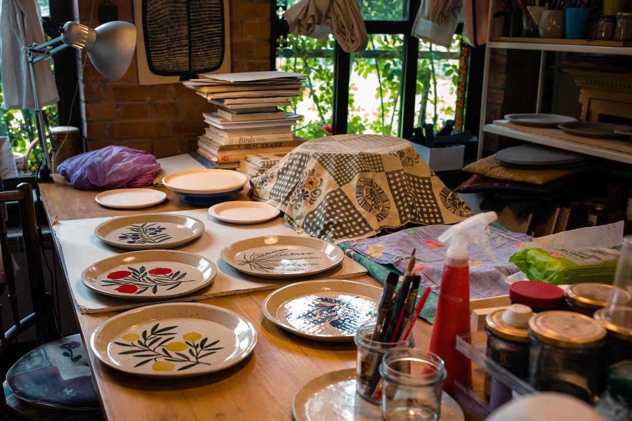 Spațiu de lucru cu discuri de ceramică și materiale de pictură pe o masă.