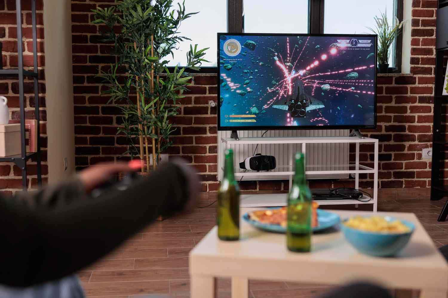 Cameră de zi cu televizor pe care rulează un joc video, masă cu gustări și băuturi