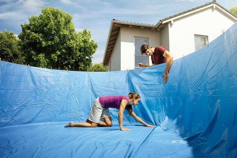 Instalarea unei folii de piscină într-o piscină de către două persoane.