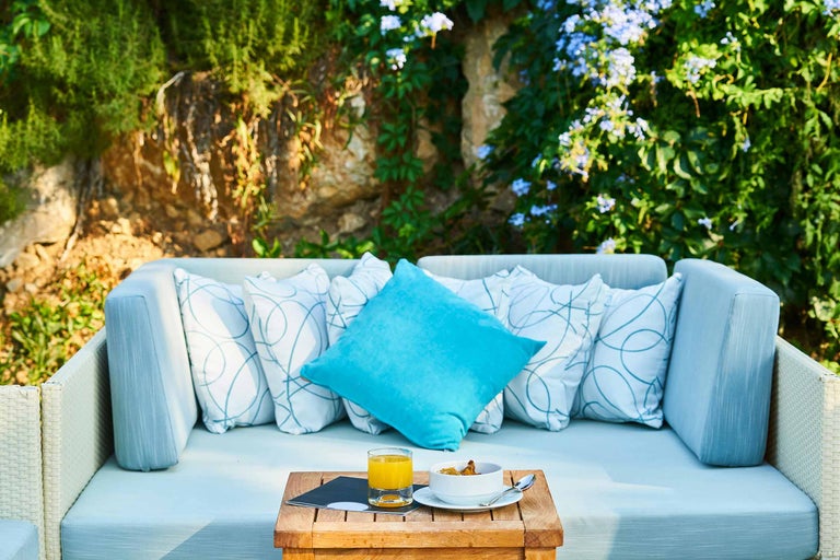 Scenă de grădină cu canapea, perne și măsuță laterală cu băuturi și mâncare.