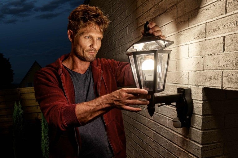 Bărbat fixând o lampă de exterior pe un perete de cărămidă.