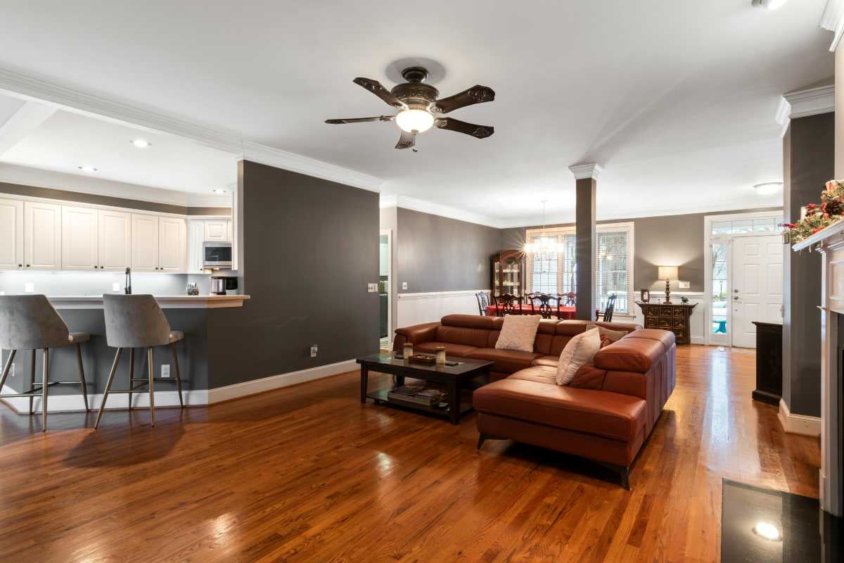 Spațiu de zi generos, deschis, cu parchet din lemn, canapea mare din piele, bucătărie modernă cu bar și ventilator de tavan cu iluminare.