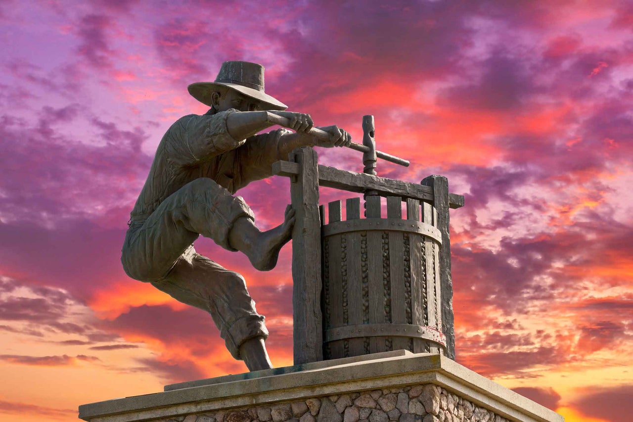 Statuia unui bărbat care operează un teasc de vin, pe un soclu de piatră