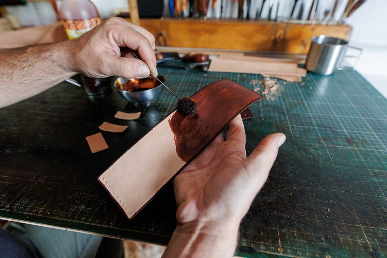 Un artizan colorează o bucată de piele cu o pensulă