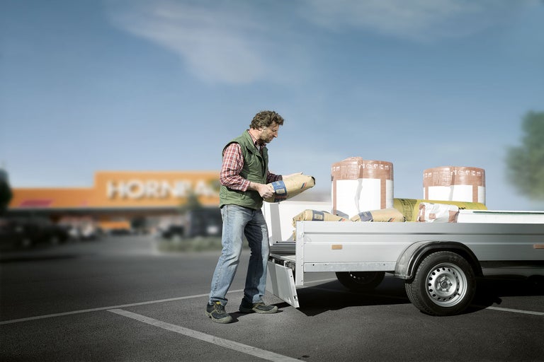 Un bărbat încarcă saci de ciment pe o remorcă în fața magazinului Hornbach.