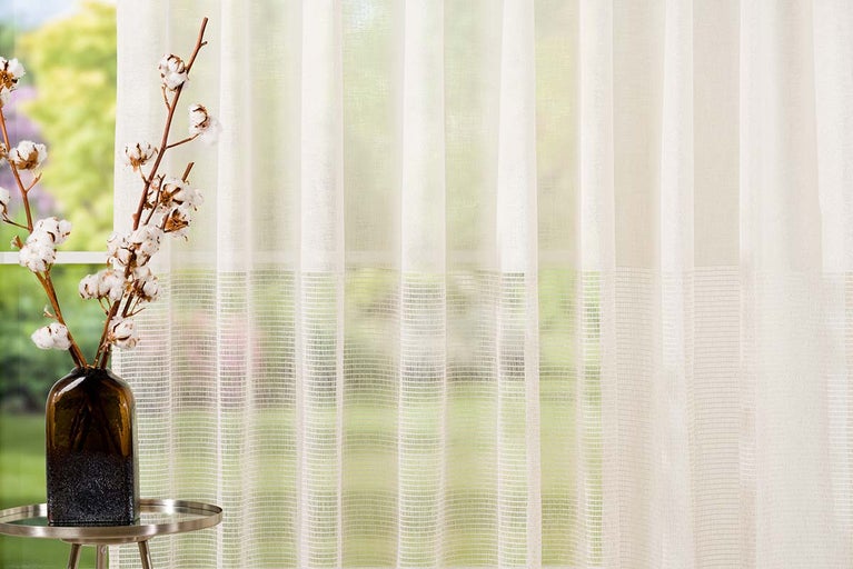 Fulare decorative cu aspect transparent și ramură de bumbac într-o vază pe o măsuță laterală în fața ferestrei.