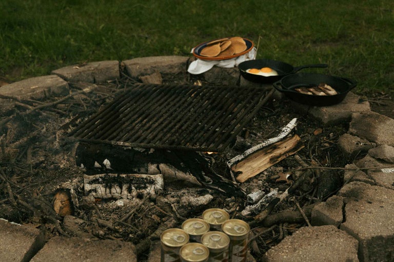 Loc de foc de tabără cu grătar, clătite, ouă, carne și cutii de băutură