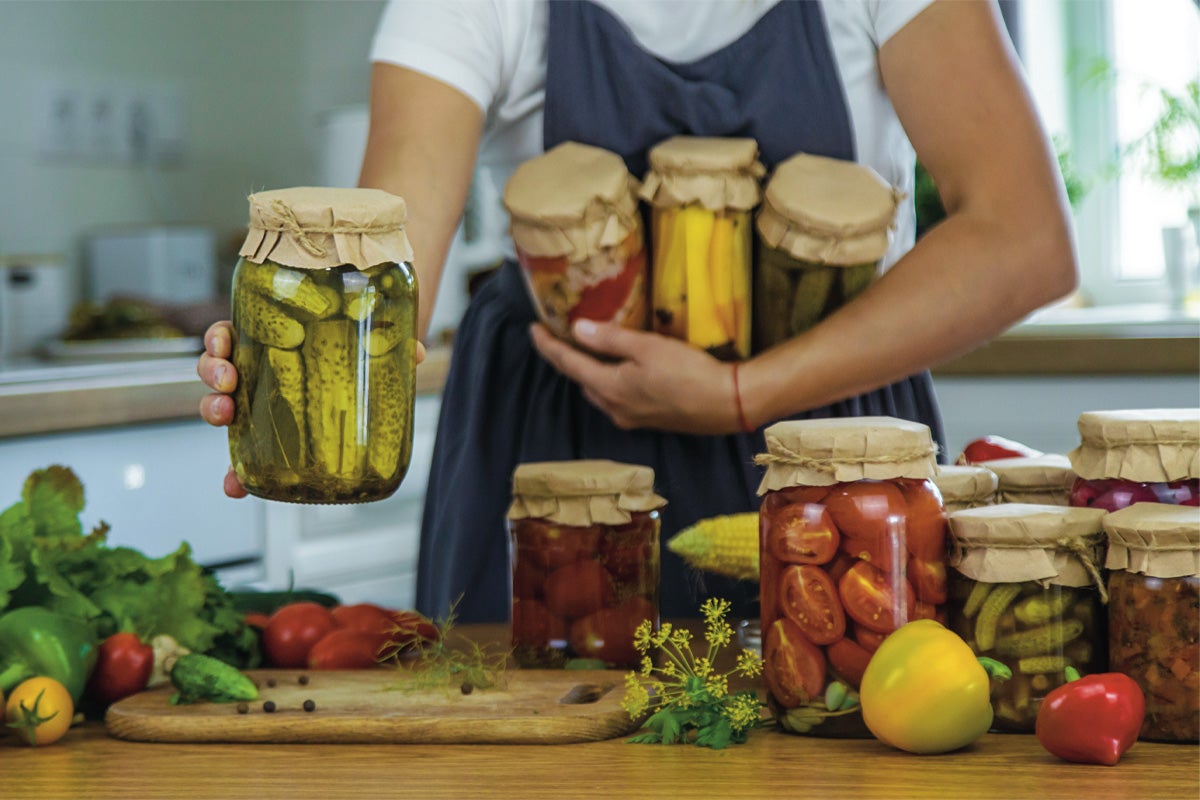 O persoană ține borcane cu legume murate pe un blat de lemn în bucătărie pentru depozitarea alimentelor.