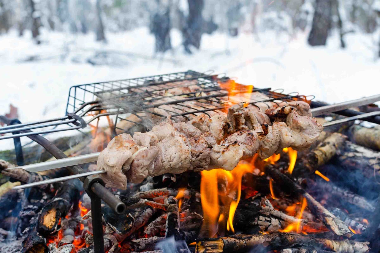 Frigărui de carne preparate la grătar pe foc deschis într-un peisaj de iarnă înzăpezit.