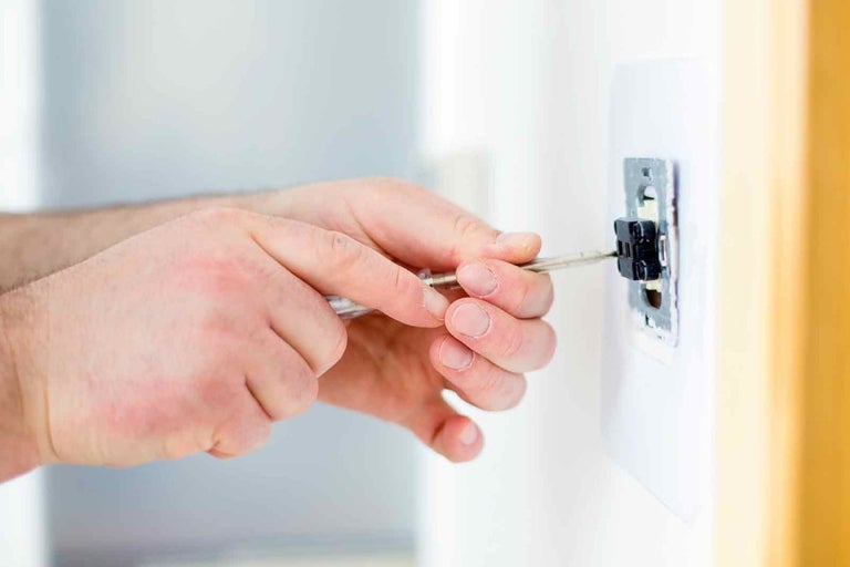 Un electrician fixează o priză cu o șurubelniță.