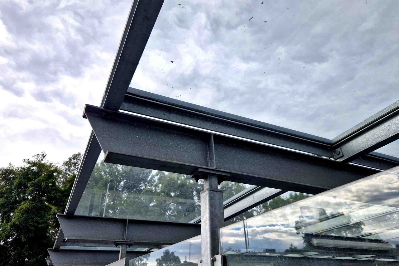 Vedere detaliată a unui acoperiș modern pentru terasă cu grinzi din oțel gri și plăci din sticlă transparentă.